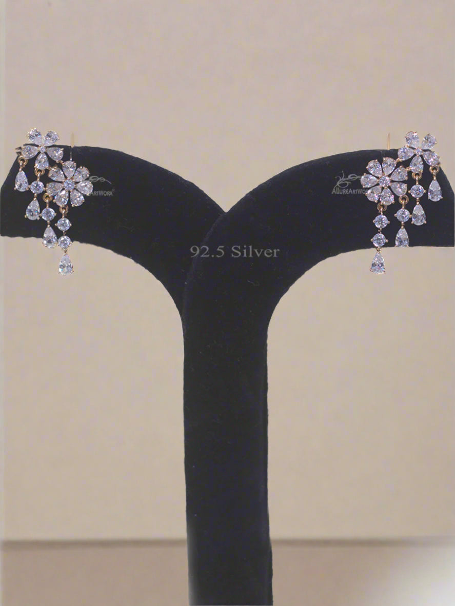 Pair of silver earrings with floral design on a black stand against a light background